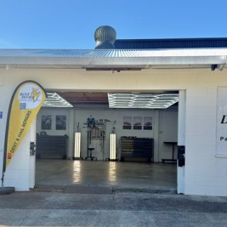 Dent Devils North Shore workshop exterior with roller door open and branded flag signage